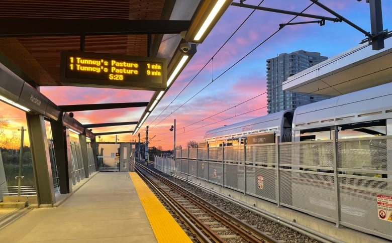 A light rail train at a station at sunrise.