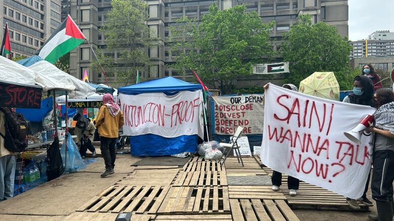 banners are hung along a fence surrounding a group of tents