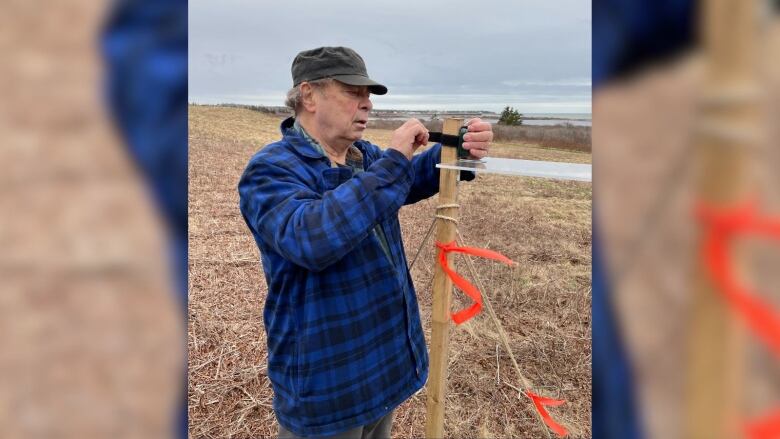 A man wearing outdoor apparel examines a survey stake in a field