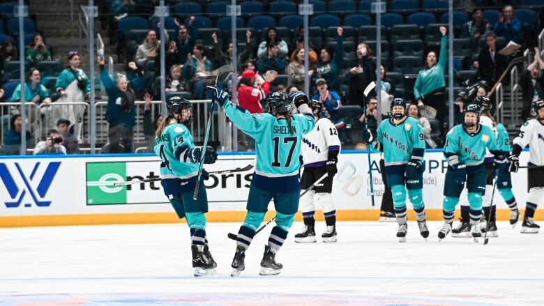 Hockey players in teal jerseys that say New York on the front celebrate on the ice.