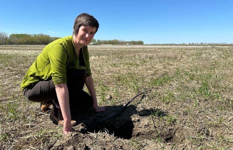 A woman kneels near a hole in a filed with a piece of long, black plastic.