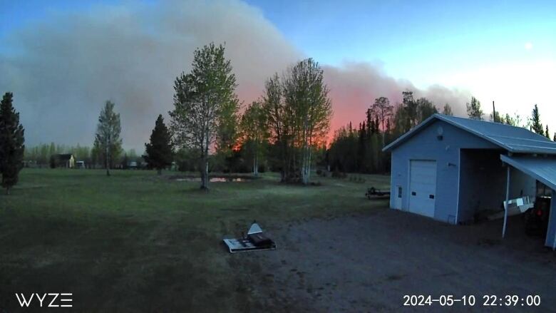 Plumes of red and grey smoke rise from behind a backyard and a shed.