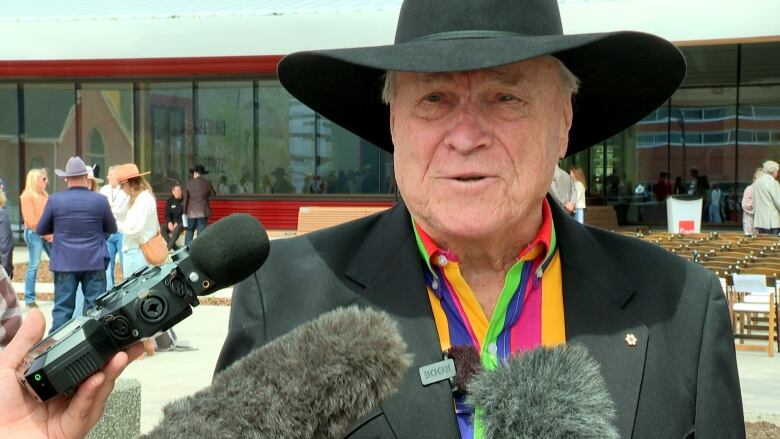 A man in a black cowboy hat and a striped shirt looks at the camera. 