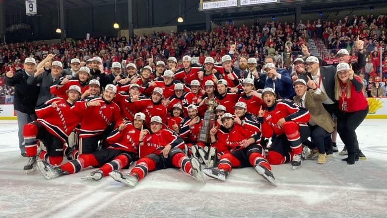 A hockey team in red jerseys poses on the ice with a large trophy cup.