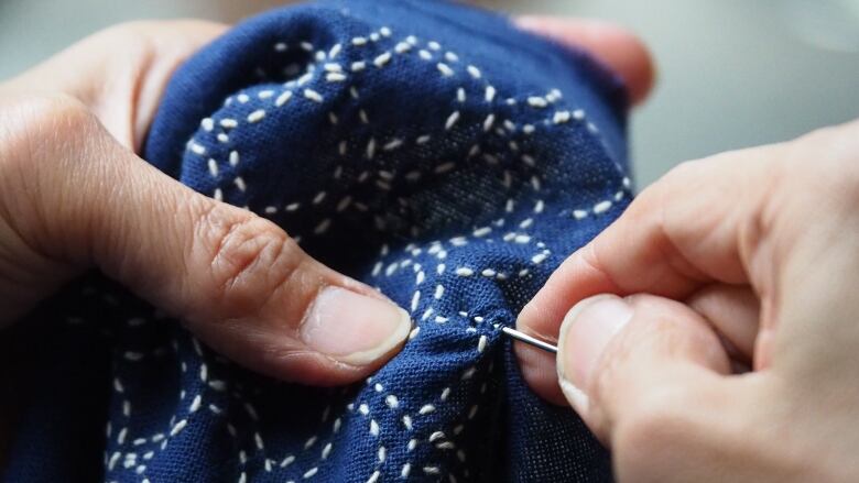 Hands holding blue fabric and using a needle to make white stitches in an artistic way