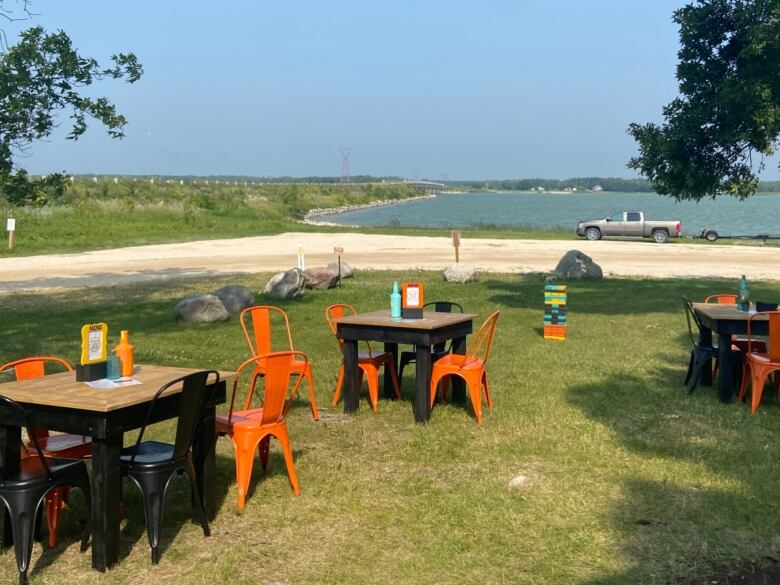 Picnic tables are seen on the grass by a lake.