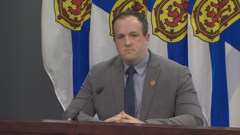 A man in a suit and tie sits at a podium.