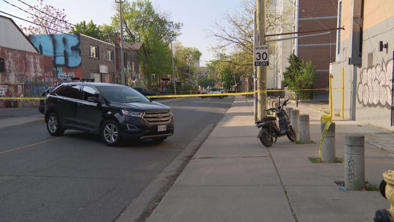 Photograph of a street showing a car with an e-bike close to it surrounded in police tape. 