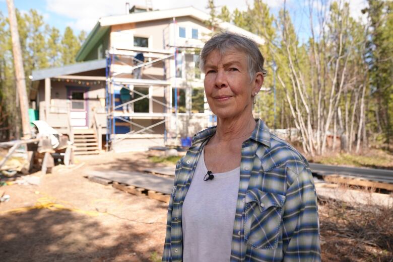 A woman stands outside, with a big house in the background.