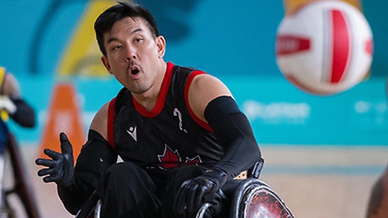 Sitting in his wheelchair with his mouth open and wearing a red and black jersey, a Canadian men's rugby player holds out his right hand to receive a pass during game action at the 2023 Parapan Am Games in Santiago, Chile.