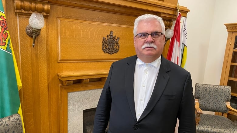 A man with a white moustache, wearing a suit, poses for a photograph.