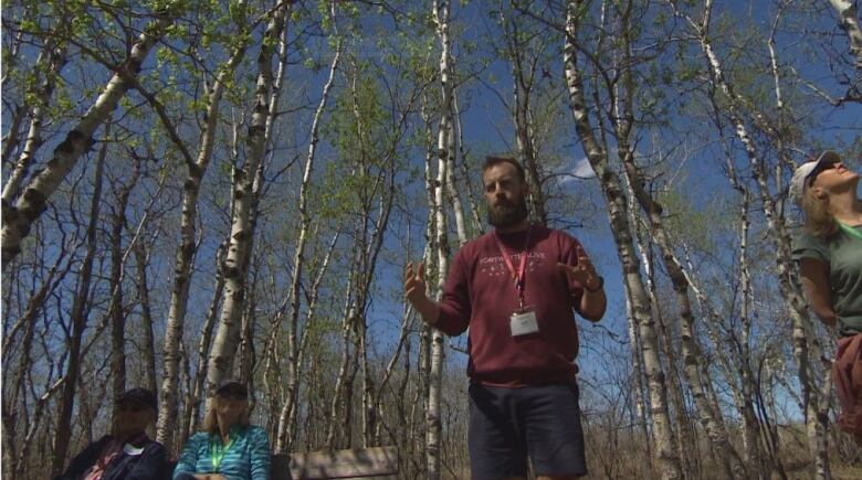 A man stands and gestures in a forest.