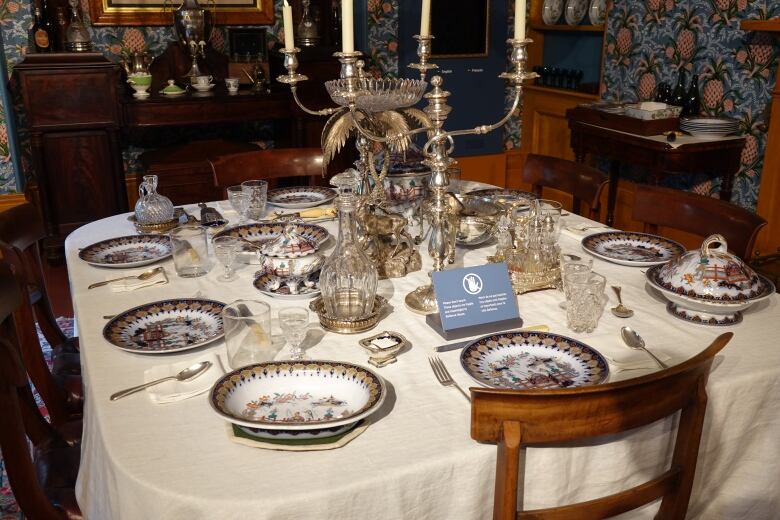 A table with fancy place settings is seen in a room with blue wallpaper covered in a pineapple design.