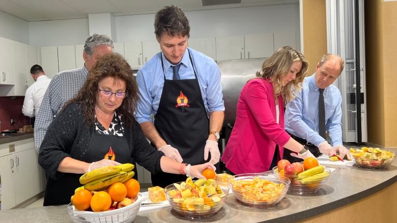 People stand at a counter, putting fruit into lunches