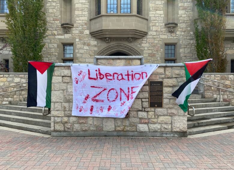 Two Palestinian flags and a handmade poster reading Liberation Zone hang on a pillar in front of the U of S administration building.