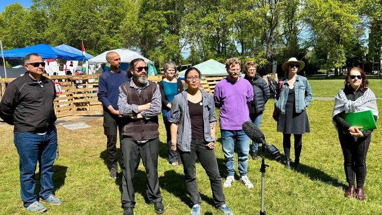 Nine people stand on the grass in front of an encampment