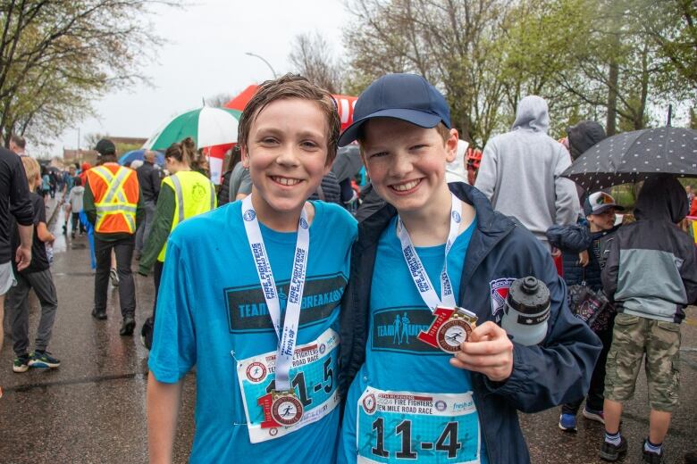 Two young people are seen smiling at a race with medals around their necks.