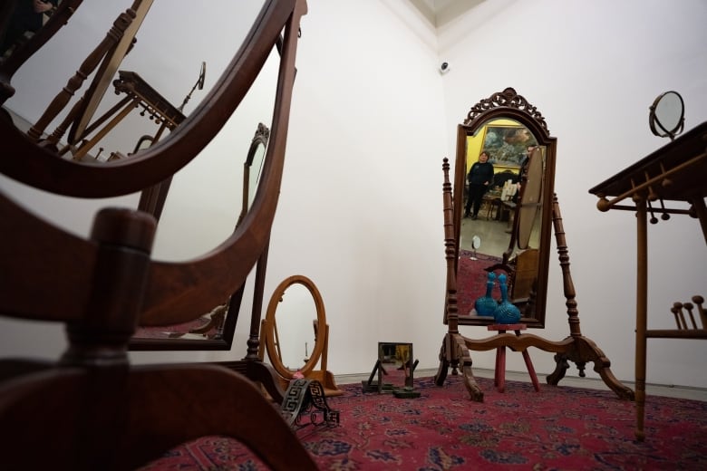 A person is reflected in one of several large antique mirrors 