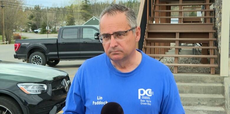 A man wearing a blue T-shirt stands in a parking lot.