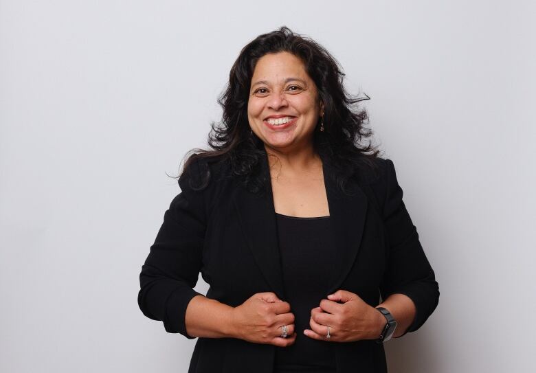 A person in a blazer stands before a white backdrop. 