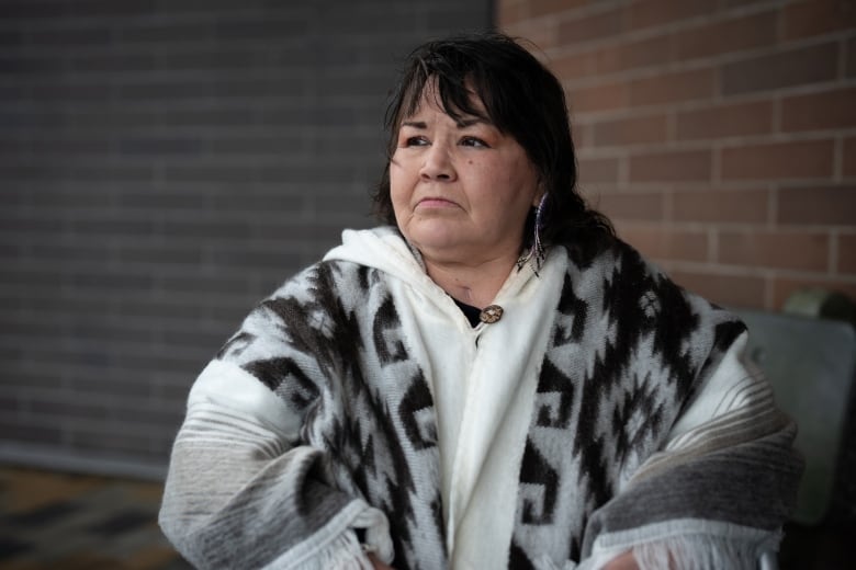 An Indigenous woman wearing a white dress looks away from the camera.