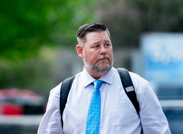 A man in a blue tie and light dress shirt outside on a sunny spring day.