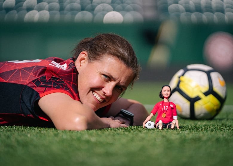 A woman lies on the grass beside a doll and a soccer ball.