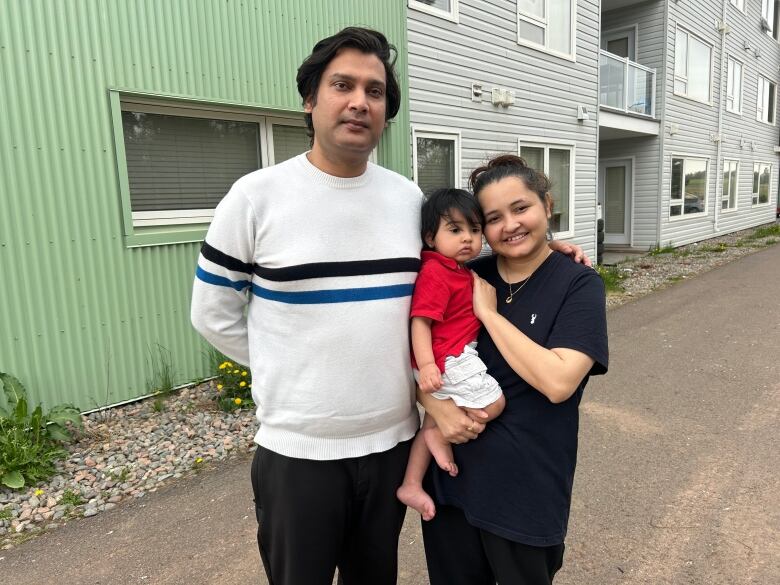 Man, woman and child on street. Woman is holding child in her arms.