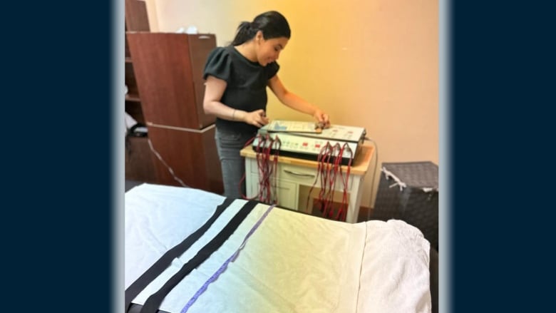 A picture of a woman beside a machine with a bed beside her and wires coming out of the machine. 