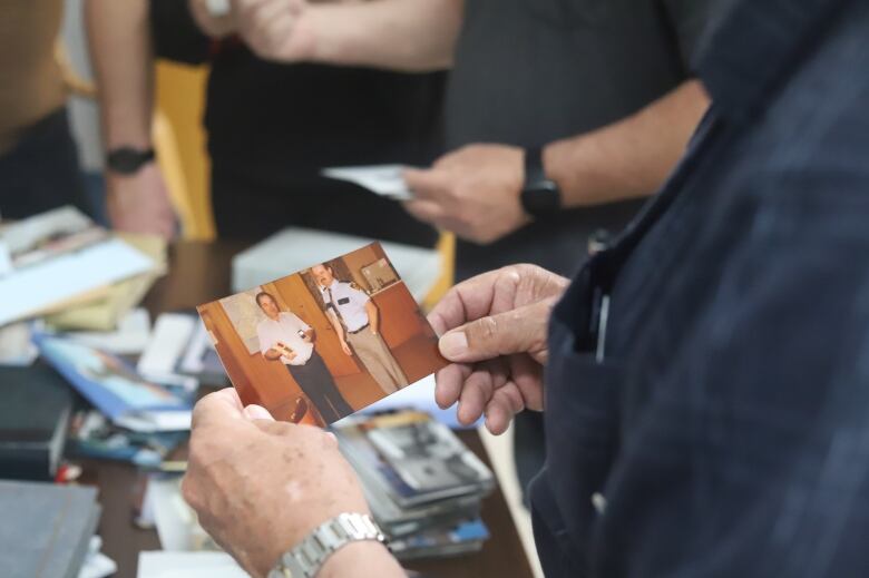 A man holds a photo of two men, one holding an award.