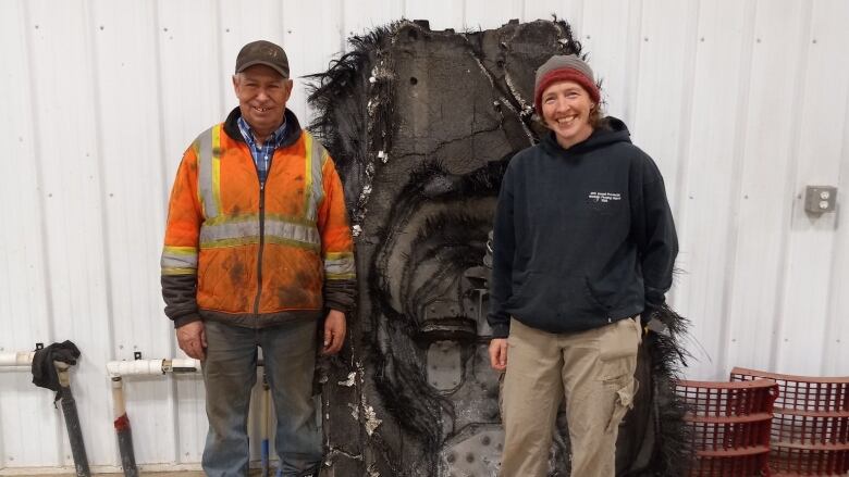 A man and woman stand on either side of a large, black piece of debris.