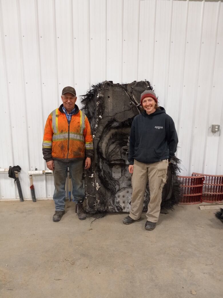 A man and woman stand on either side of a large, black piece of debris.