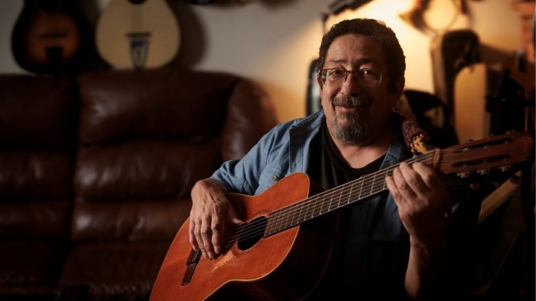 A man wearing a blue button-down shirt holds a guitar. 