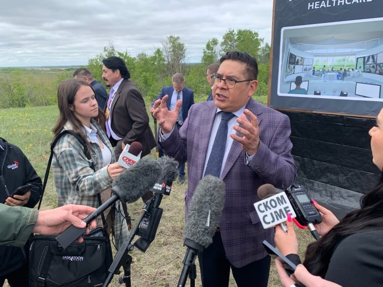 A man stands in front of microphones and speaks to reporters outdoors.