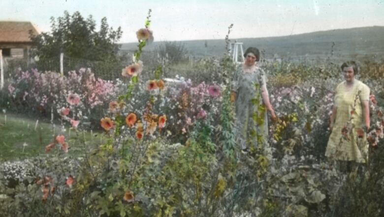 Colourized photo of blooming flowers, with two women, wearing dresses, in the background