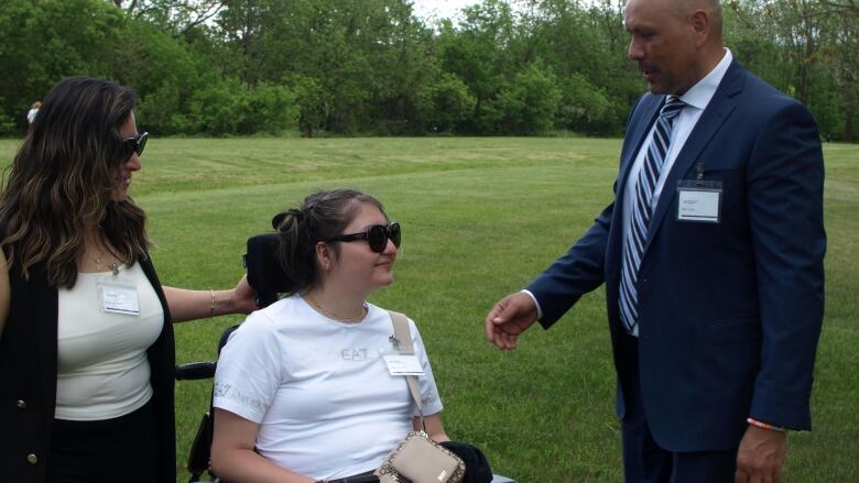 Two adults stand with their 17-year-old daughter, who is seated at centre in a wheelchair. 