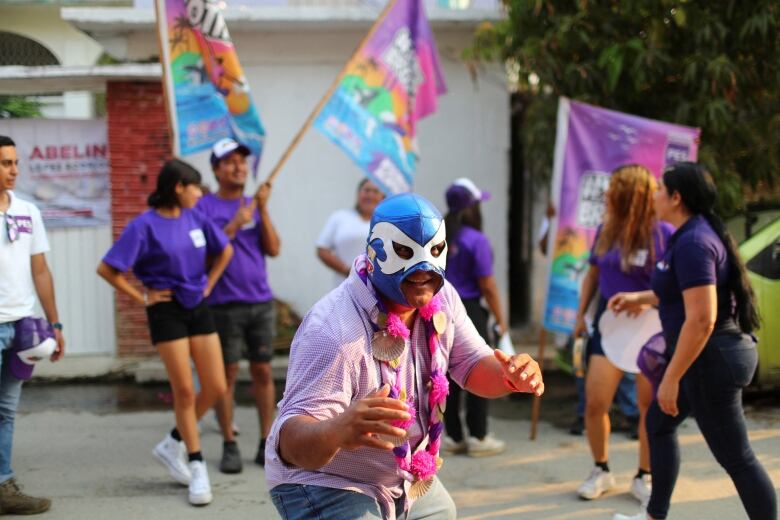 A man in a blue wrestling mask and pink shirt at an election event.