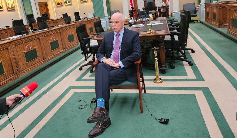 A man wearing a suit sits in a chair inside the House of Assembly.