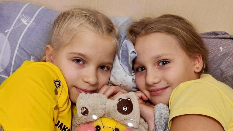 Two girls cuddle against pillows with a stuffed animal