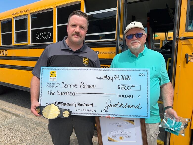 Two men stand in front of a yellow school bus.