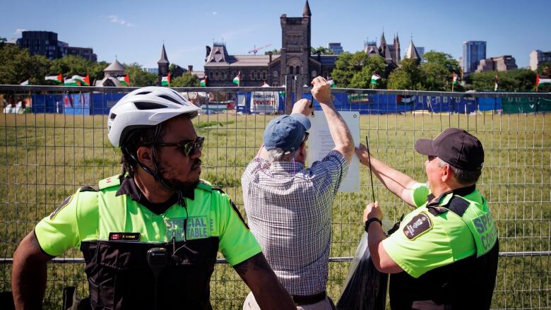 A university staff person, escorted by campus security, puts up trespass notices on a pro-Palestinian encampment at the University of Toronto on May 24, 2024.