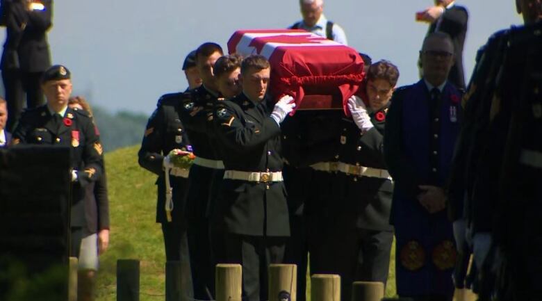 A group of military members carrying a casket draped with a Canadian flag. 