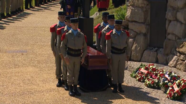 A group of military members standing over a casket near a memorial site. 