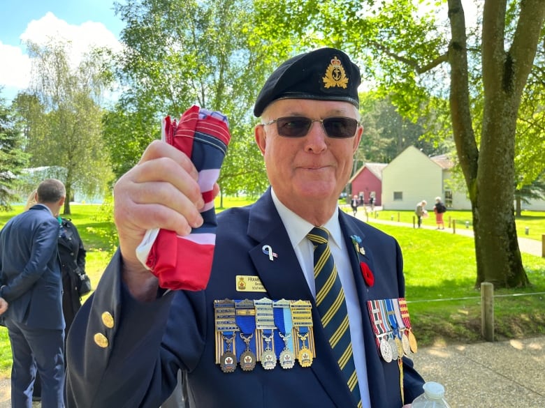 An older man wearing military fatigues holding a red and white flag. 