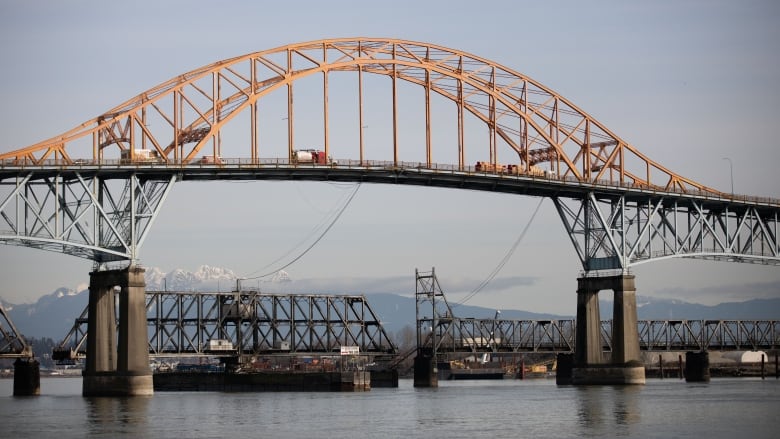 A large bridge with yellow tresses, with snow-capped mountains in the background.