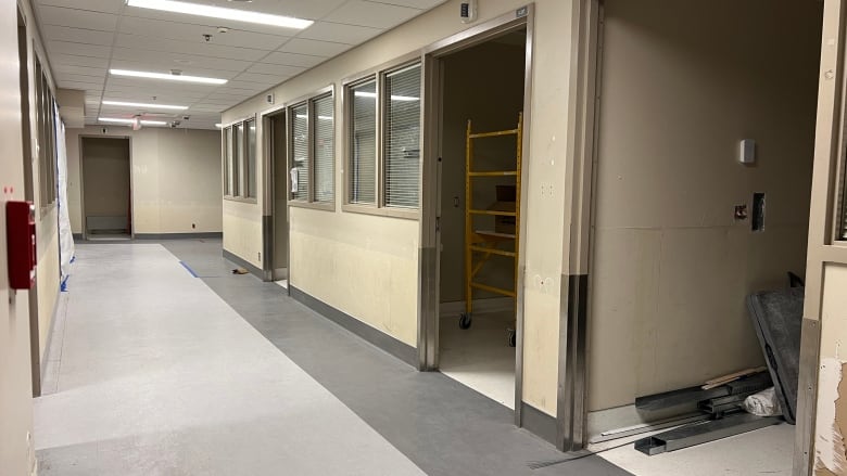 An empty hallway in a hospital with several open doors and some construction material.