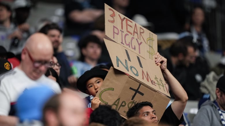 A fan holds up a sign reading '3 Year Piggy $' and 'No Messi'.