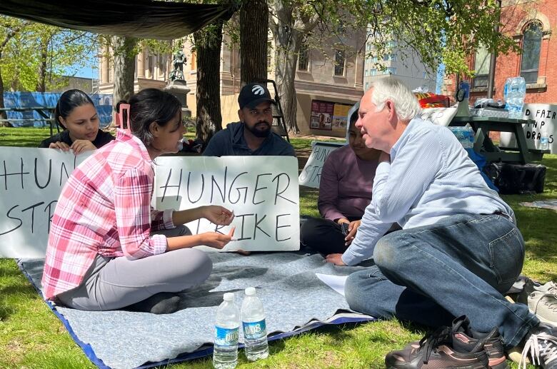 Peter Bevan-Baker sits on a blanket talking with protesters holding hunger strike signs.