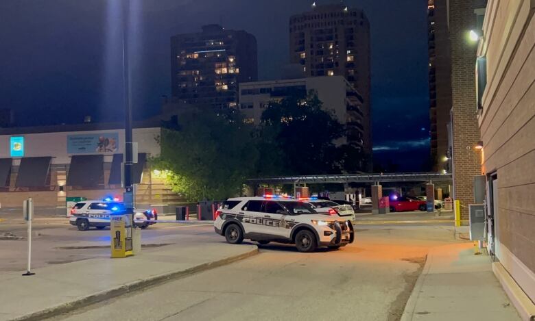 Police vehicles with their lights on are gathered in a parking lot at night.