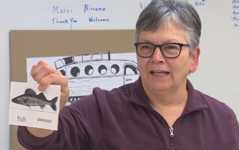 A woman with short grey hair holds up a card with a picture of a fish.